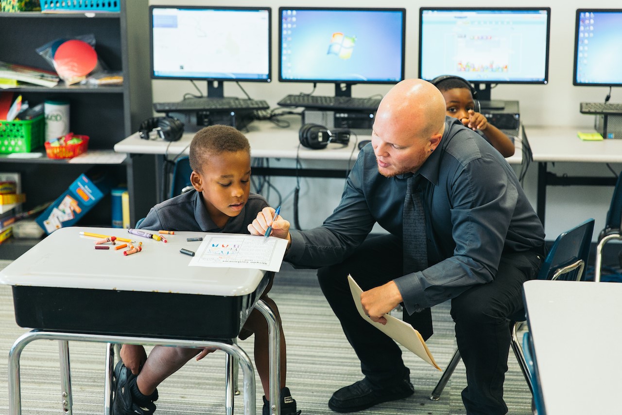 Richard Russell, one of Sugar Creek Charter's 18 curriculum specialists, helps a kindergarten student with his assignment. Photo by Noah Turley.